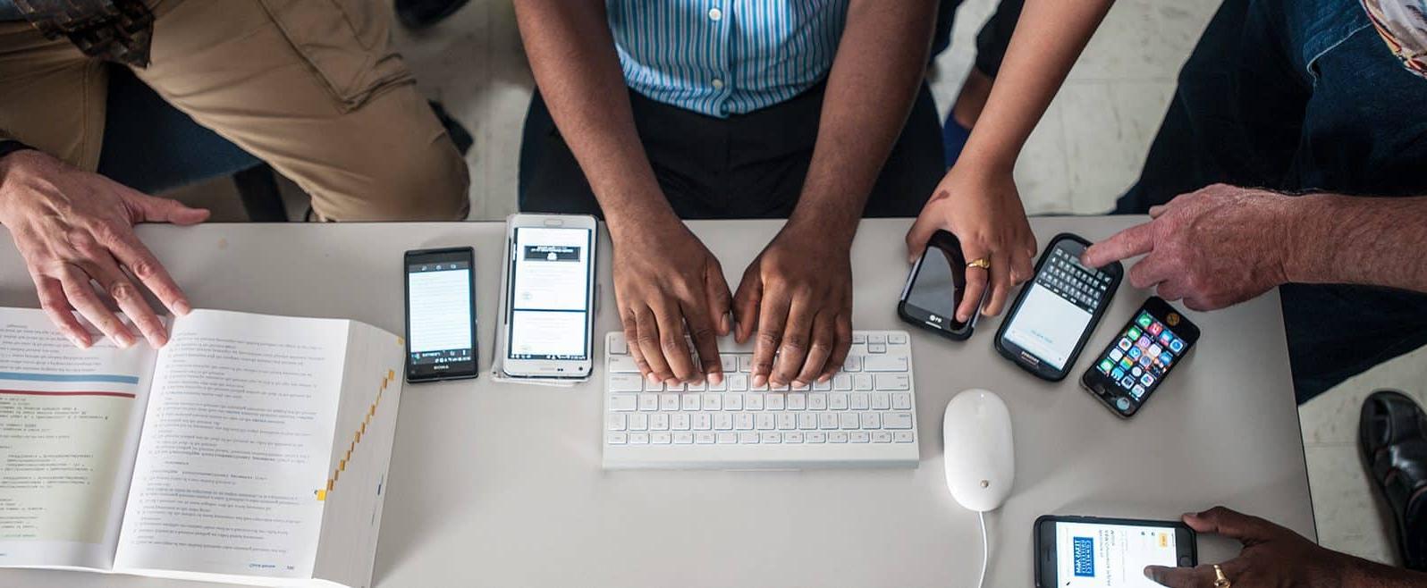 Students working at desk with cell phones, keyboard and textbook