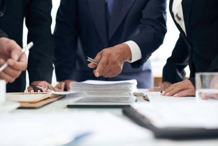 Two males and a female dressed nicely looking at legal documents.